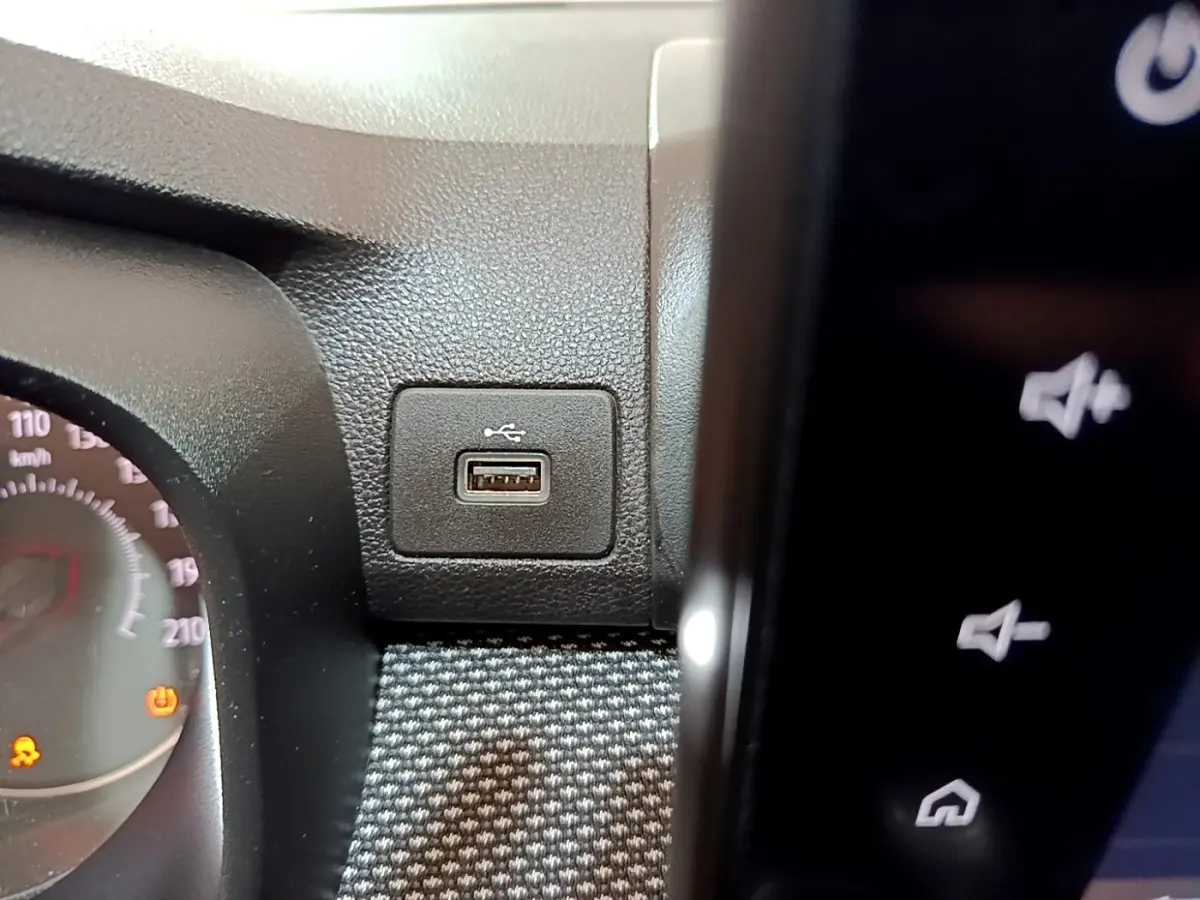 Gros plan sur la prise USB intégrée au tableau de bord noir de la Dacia Sandero blanche, côté conducteur.