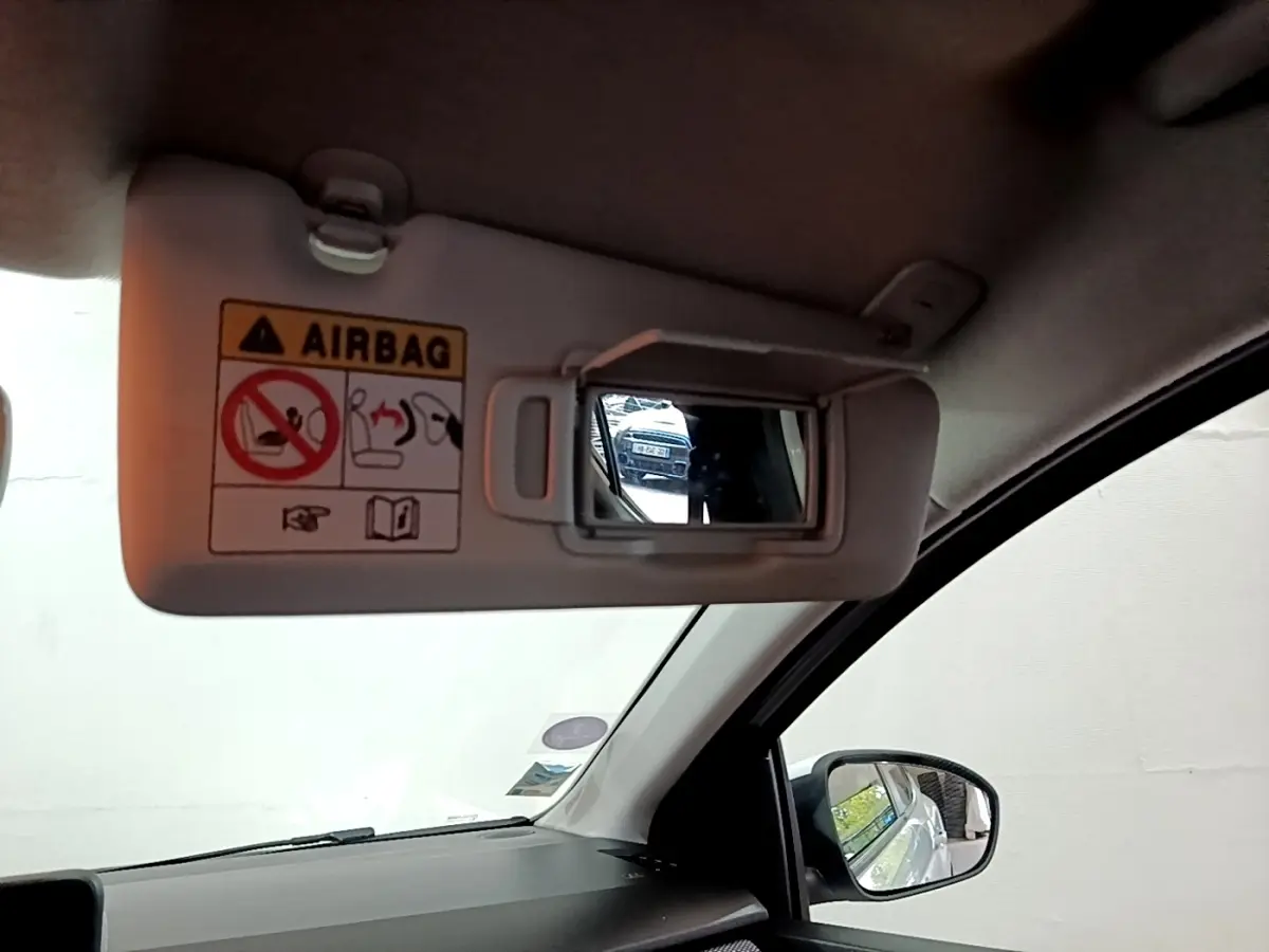 Intérieur de la Dacia Sandero blanc, vue sur le pare-soleil conducteur avec miroir et rétroviseur latéral droit.