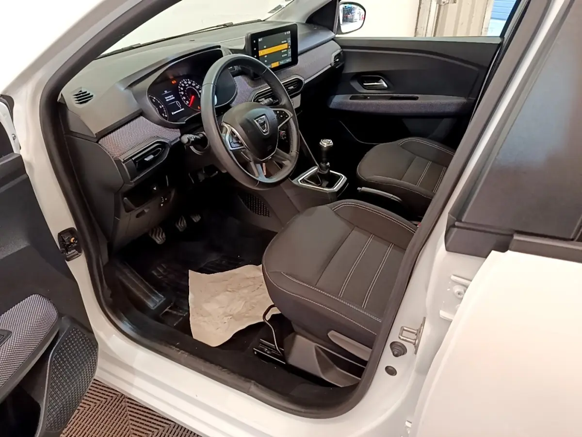 Vue intérieure côté conducteur de la Dacia Sandero blanche 2022, avec tableau de bord moderne et sièges noirs.