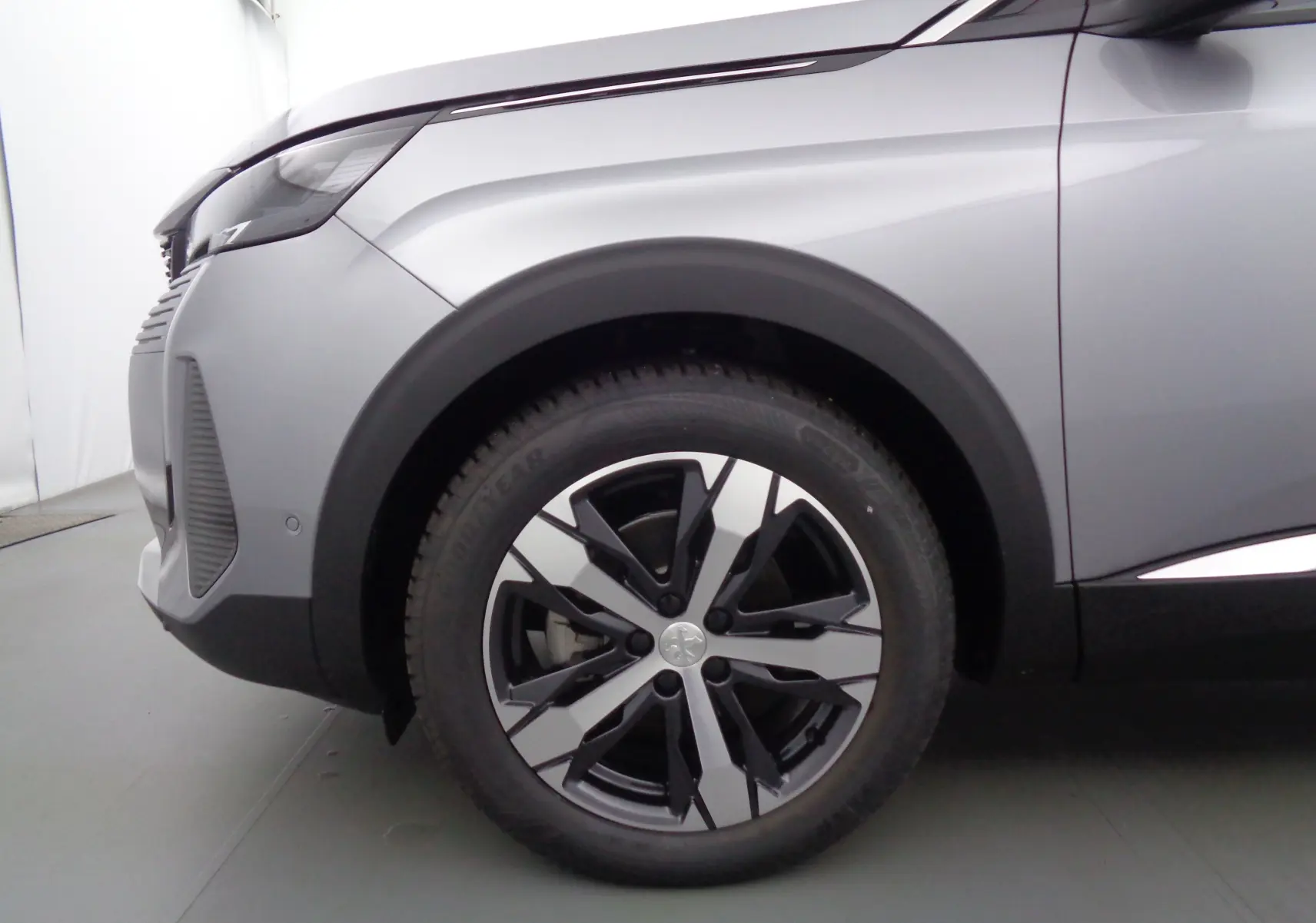 Gros plan sur la roue avant gauche et l'aile d'un Peugeot 3008 gris Artense métallisé, mettant en valeur la jante bicolore moderne.