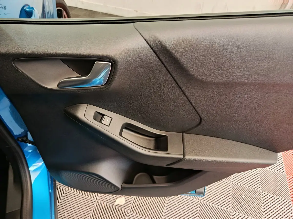 Vue rapprochée de la porte côté gauche du Ford Puma bleu 2025, avec poignée argentée et commande de vitre électrique.