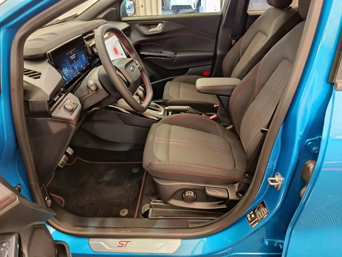Intérieur côté conducteur du Ford Puma bleu 2025, sièges noirs avec surpiqûres rouges et tableau de bord numérique.