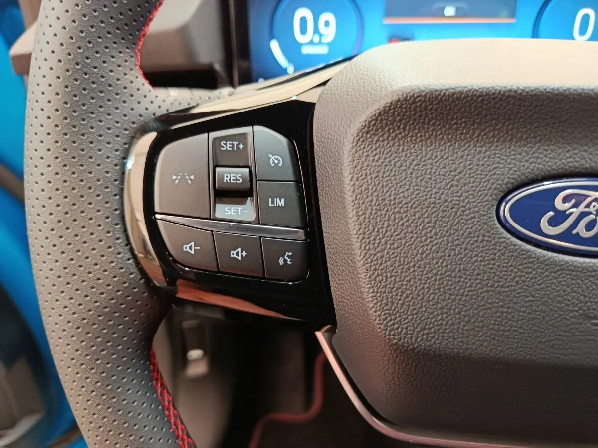 Gros plan sur la partie gauche du volant perforé avec commandes multifonctions du Ford Puma bleu 2025.
