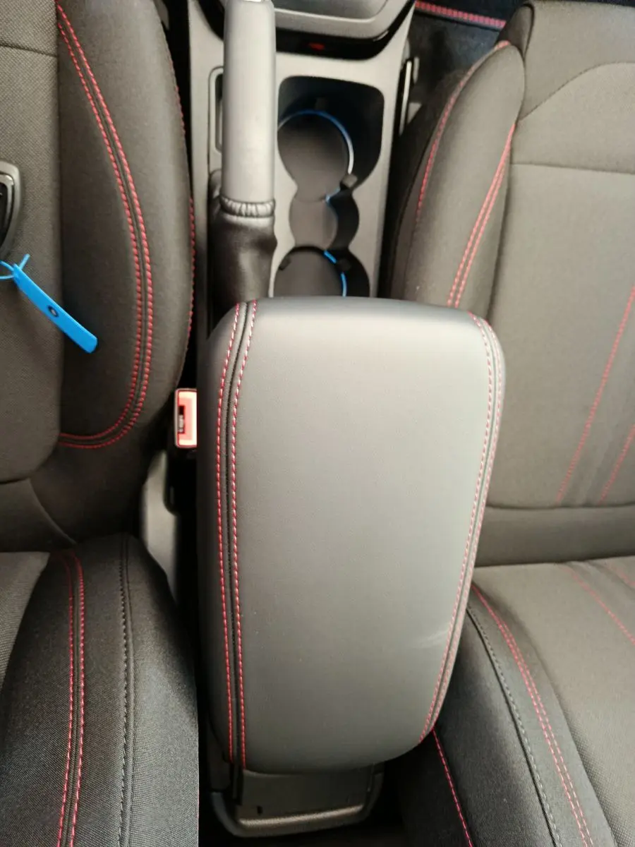 Vue plongeante sur l'accoudoir noir avec surpiqûres rouges entre les sièges avant du Ford Puma ST-LINE 2025.