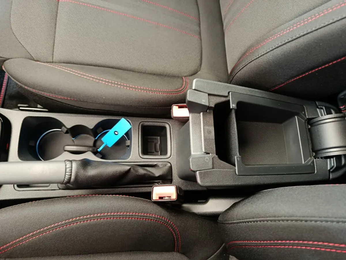 Vue plongeante sur la console centrale noire et les sièges tissu gris foncé avec surpiqûres rouges du Ford Puma 2025.