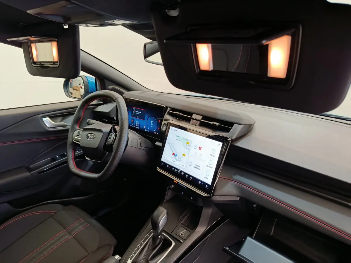 Vue intérieure côté conducteur du Ford Puma bleu 2025, tableau de bord avec écran tactile et volant cuir noir à surpiqûres rouges.
