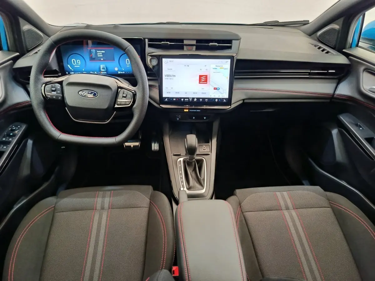 Intérieur du Ford Puma 2025 en vue frontale, tableau de bord noir avec écran tactile central et volant cuir noir à surpiqûres rouges