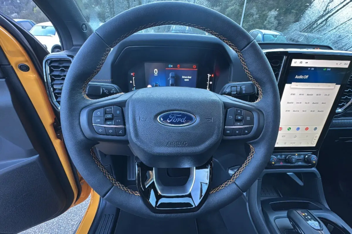 Vue centrée sur le volant avec surpiqûres orange du Ford Ranger 2025 Cyber orange, tableau de bord et écran tactile visibles.