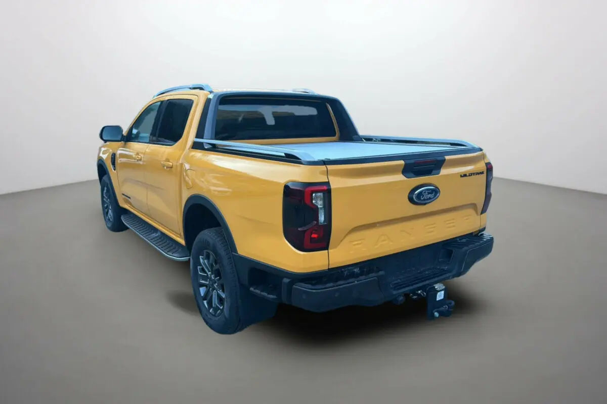 Ford Ranger 2025 Cyber orange en 3/4 arrière droit, avec benne couverte et logo Wildtrak visible sur la porte.