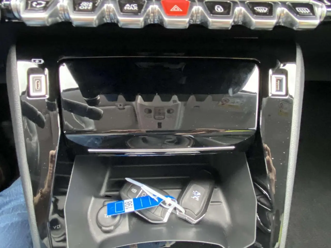 Gros plan sur la console centrale noire brillante du Peugeot 208 bleu, avec deux clés mains libres posées.