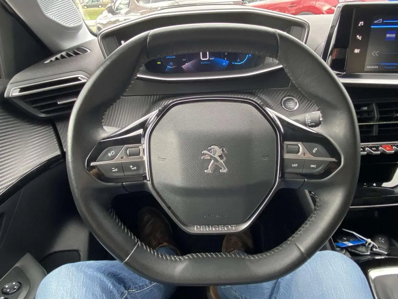 Vue rapprochée du volant cuir noir de la Peugeot 208 2020 avec commandes intégrées et tableau de bord digital.