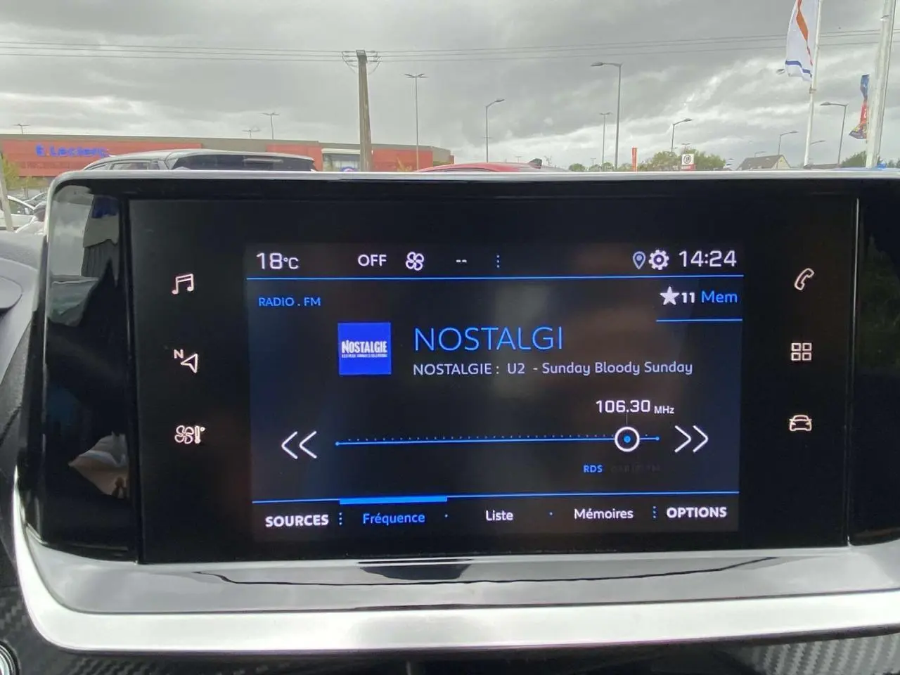 Écran tactile central de la Peugeot 208 bleu, affichant la radio sur la fréquence 106.30 MHz en intérieur véhicule.