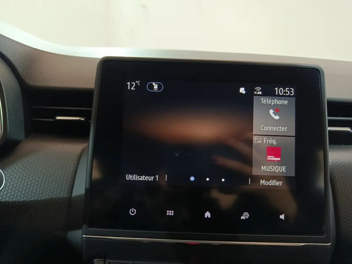 Écran tactile central affichant la température et options multimédia dans l'habitacle d'une Renault Clio blanche.