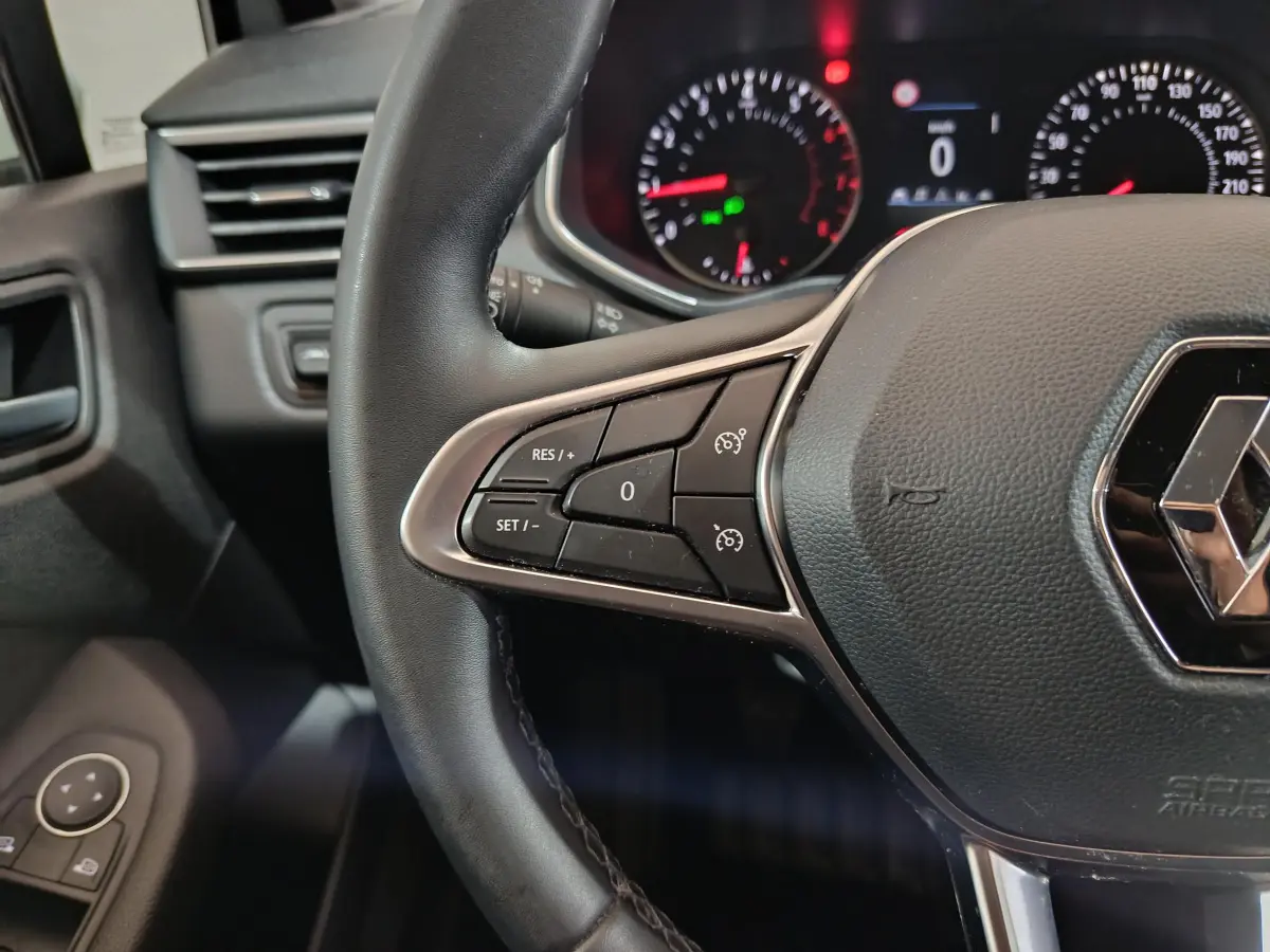 Gros plan sur le volant cuir noir de la Renault Clio Business TCe 90 2021 avec commandes intégrées et tableau de bord éclairé.