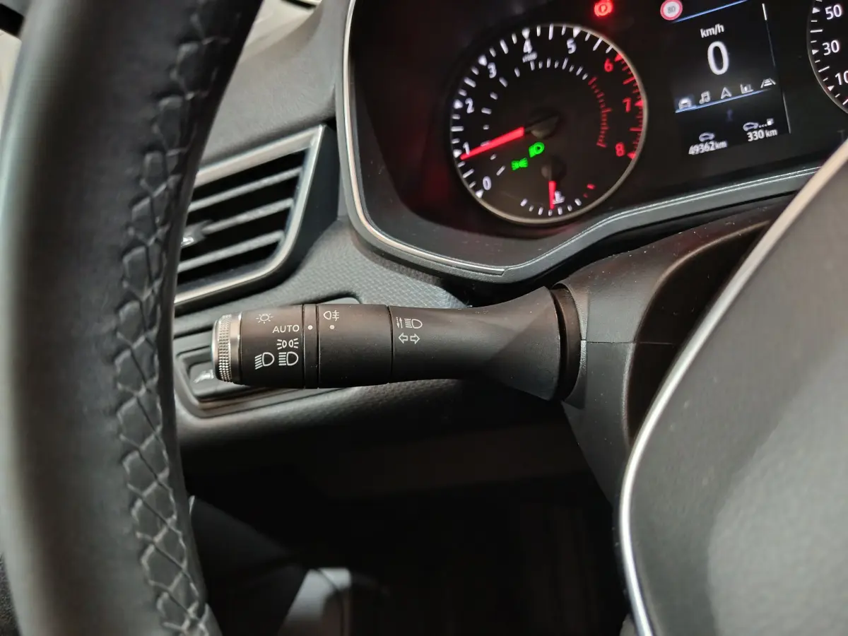 Gros plan sur la manette de phares et clignotants à gauche du volant cuir d'une Renault Clio Business blanche, tableau de bord allumé.