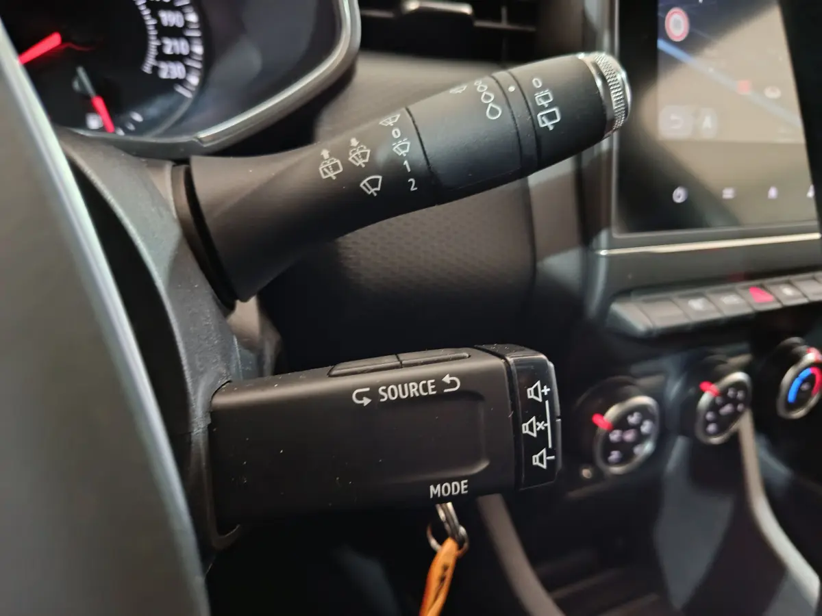 Gros plan sur la commande multifonction à gauche du volant dans l’habitacle noir de la Renault Clio Business blanche 2021.