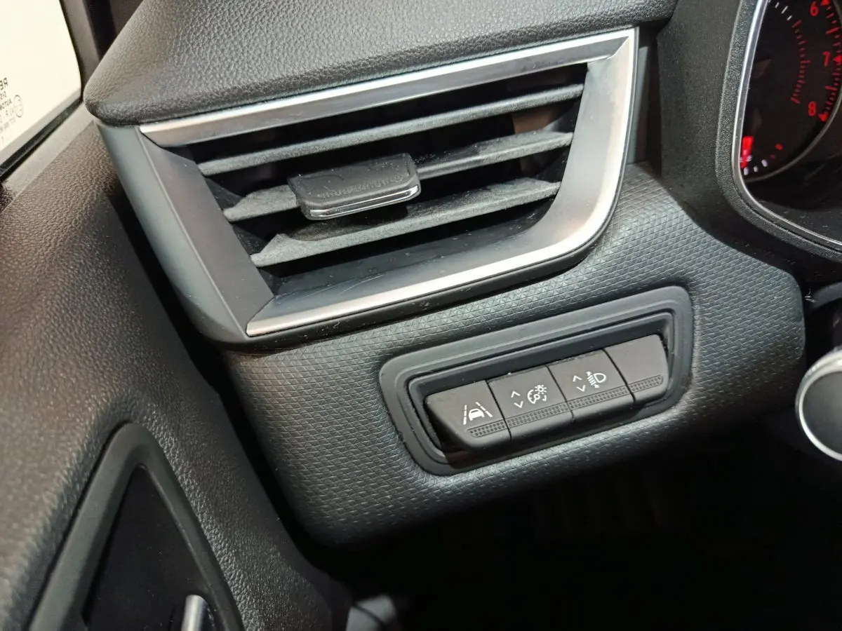 Gros plan sur la console gauche du tableau de bord noir de la Renault Clio Business TCe 90 avec commandes d'assistance et ventilation.