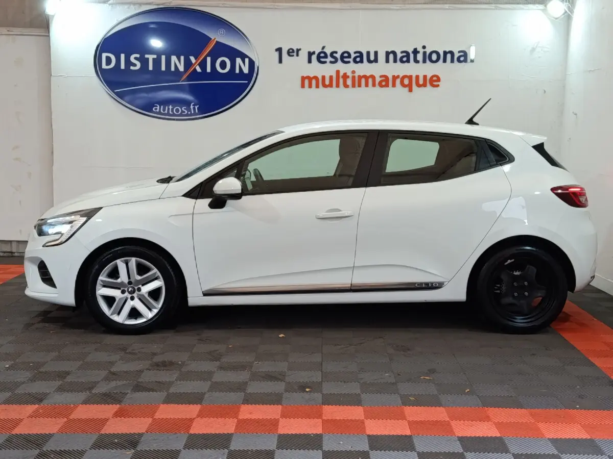 Profil côté gauche d'une Renault Clio Business TCe 90 blanche 2021 avec jantes avant argent et arrière noires, en intérieur showroom.