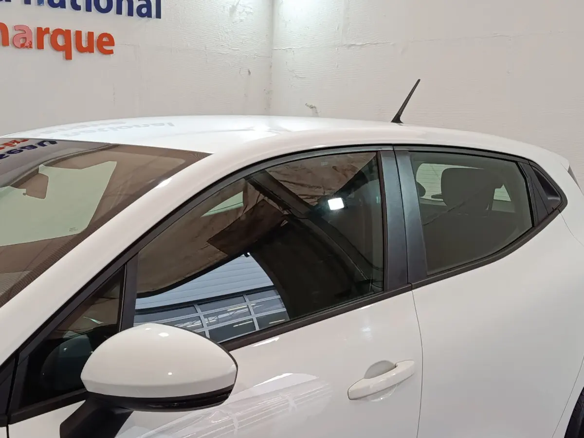 Profil côté gauche d'une Renault Clio Business TCe 90 blanche, avec rétroviseur et antenne visibles sur fond intérieur.