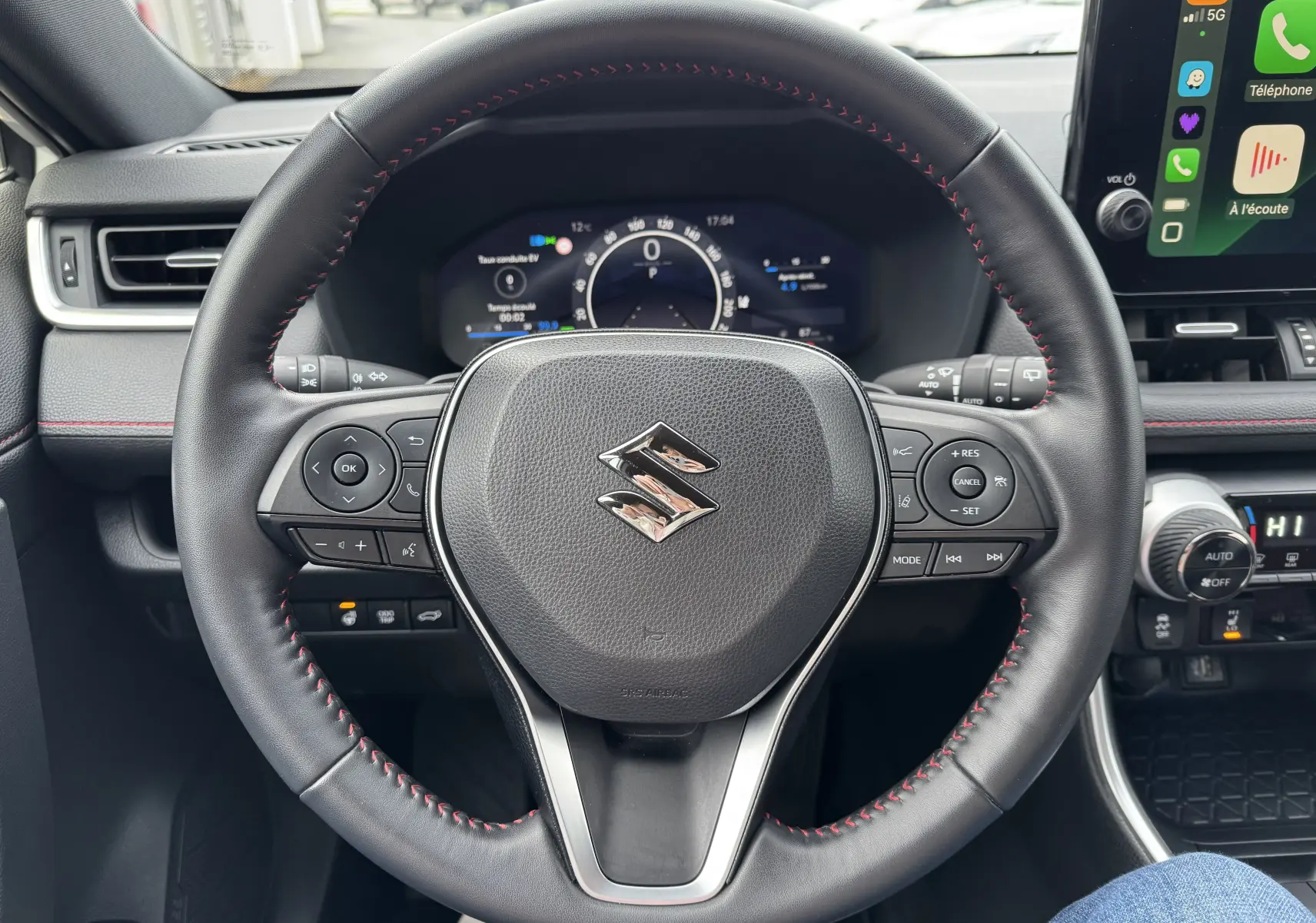 Vue rapprochée du volant en cuir noir avec surpiqûres rouges du Suzuki Across hybride rechargeable 2023, tableau de bord numérique visible.