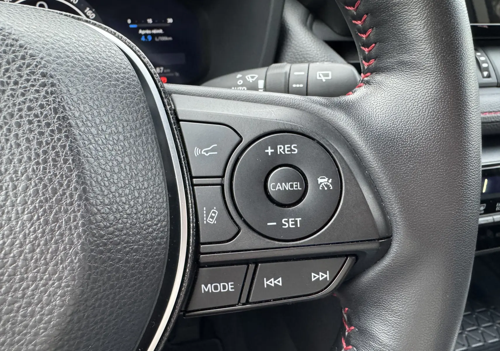 Gros plan sur les commandes du volant noir avec surpiqûres rouges du Suzuki Across hybride rechargeable 2023.