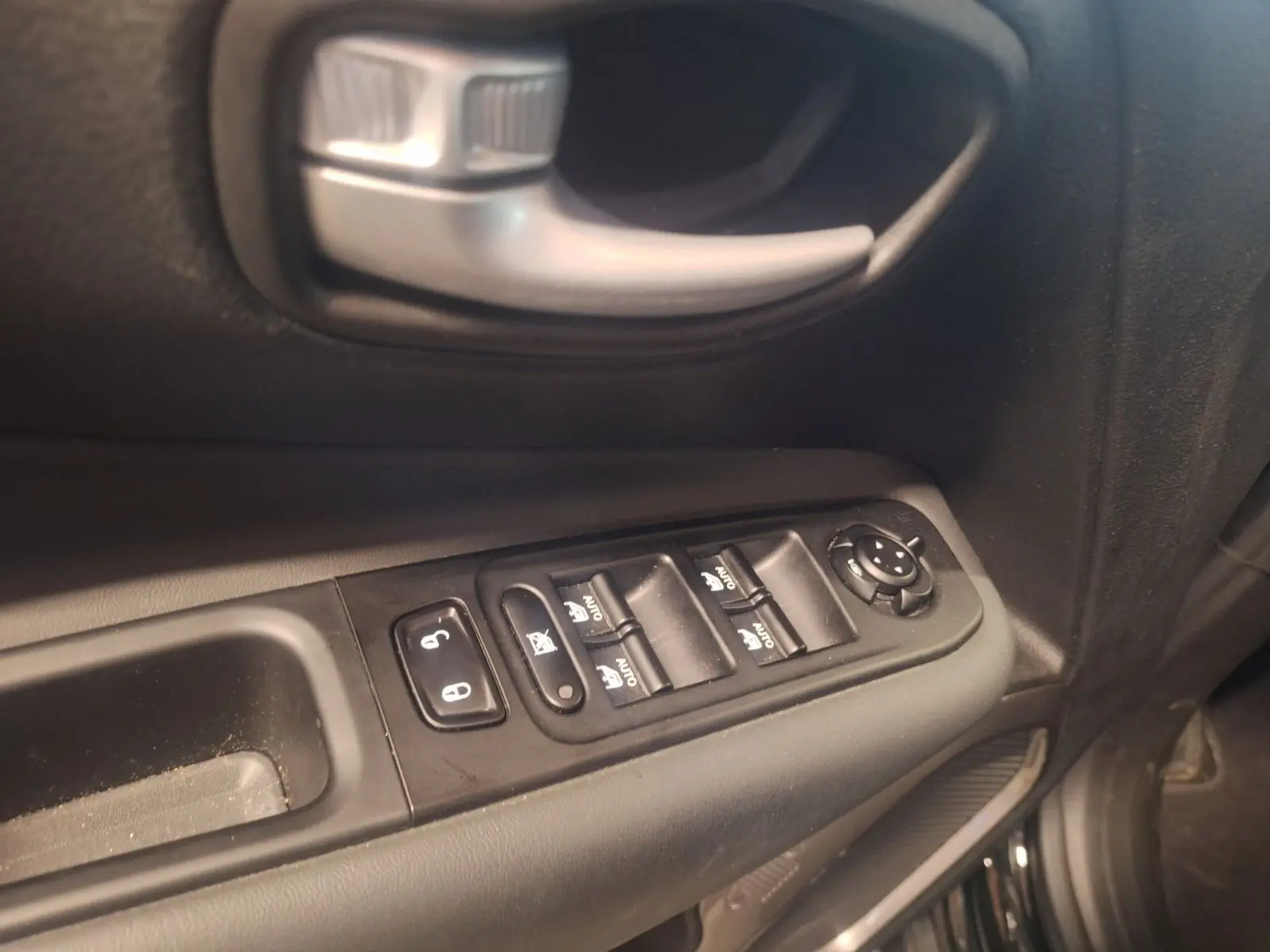 Gros plan sur la commande des vitres et la poignée intérieure côté gauche d’un Jeep Renegade noir 2024.