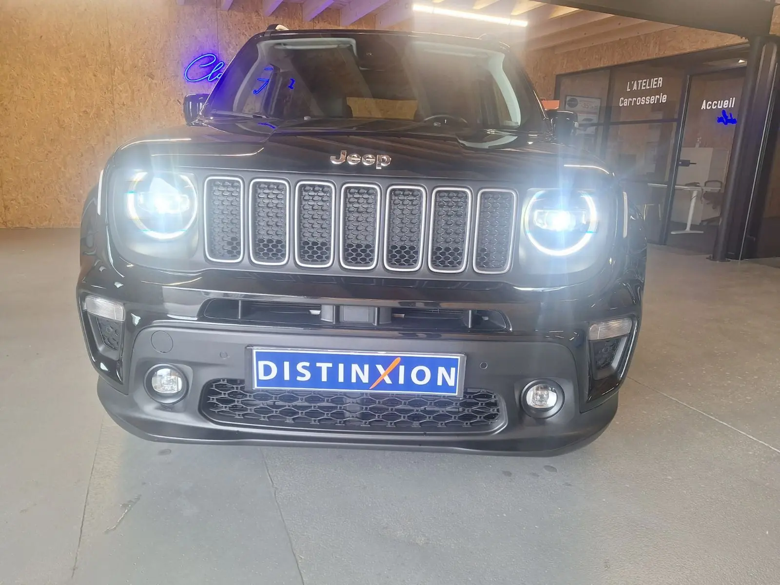 Vue de face d'un Jeep Renegade noir 2024 avec phares allumés et calandre à sept barres dans un showroom.