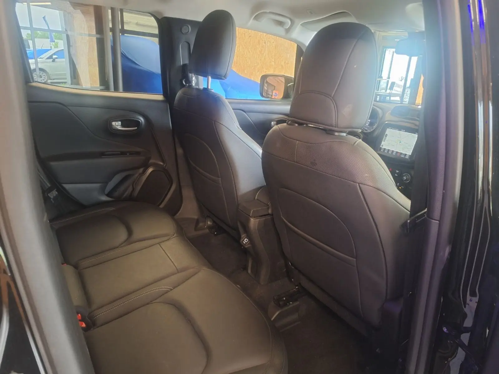 Vue intérieure arrière du Jeep Renegade 2024 noir, sièges en cuir noir et tableau de bord avec écran tactile visible à l'avant.