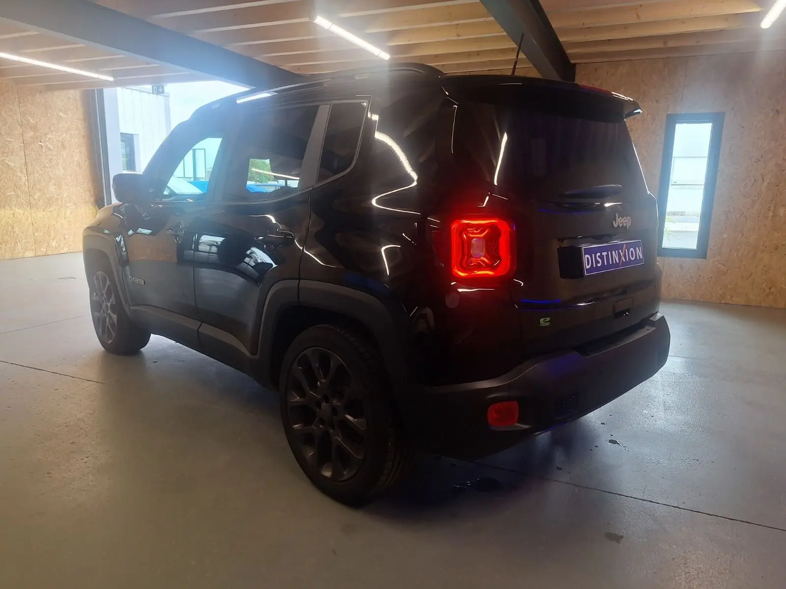 Jeep Renegade noir en 3/4 arrière droit dans un garage, avec feux arrière allumés et jantes foncées.