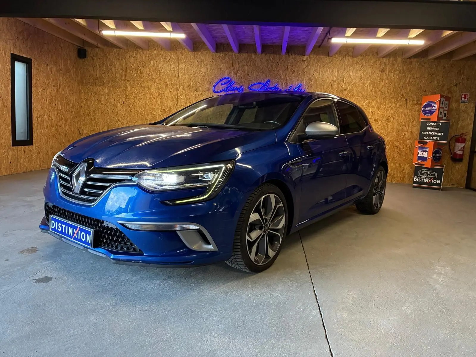Renault Mégane 1.7 BlueDCI 150 GT Line bleu vue 3/4 avant droit en intérieur avec jantes alliage et phares allumés.