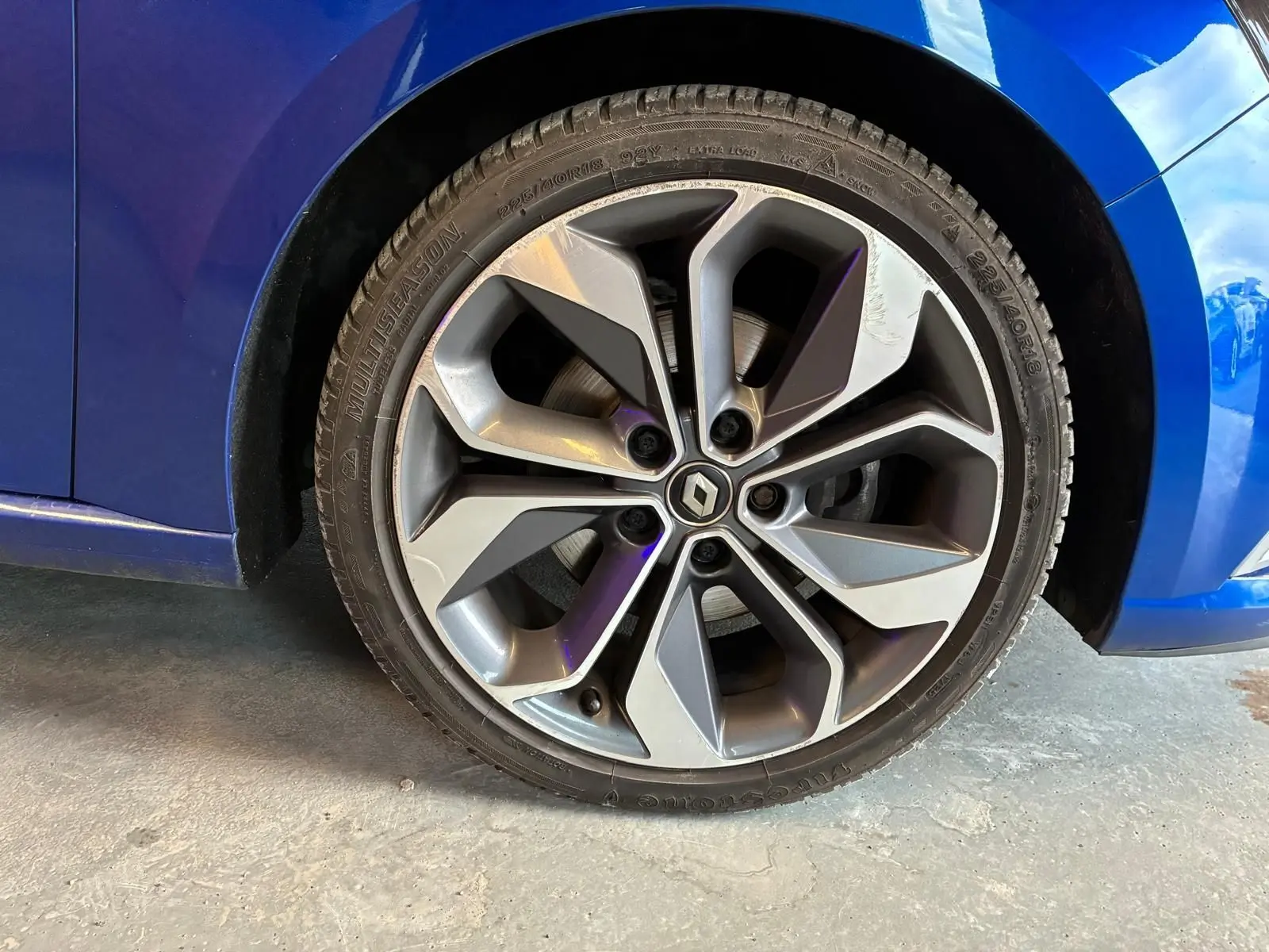 Gros plan sur la roue avant gauche d’une Renault Mégane bleu 2019 avec jante alliage gris foncé à design moderne.