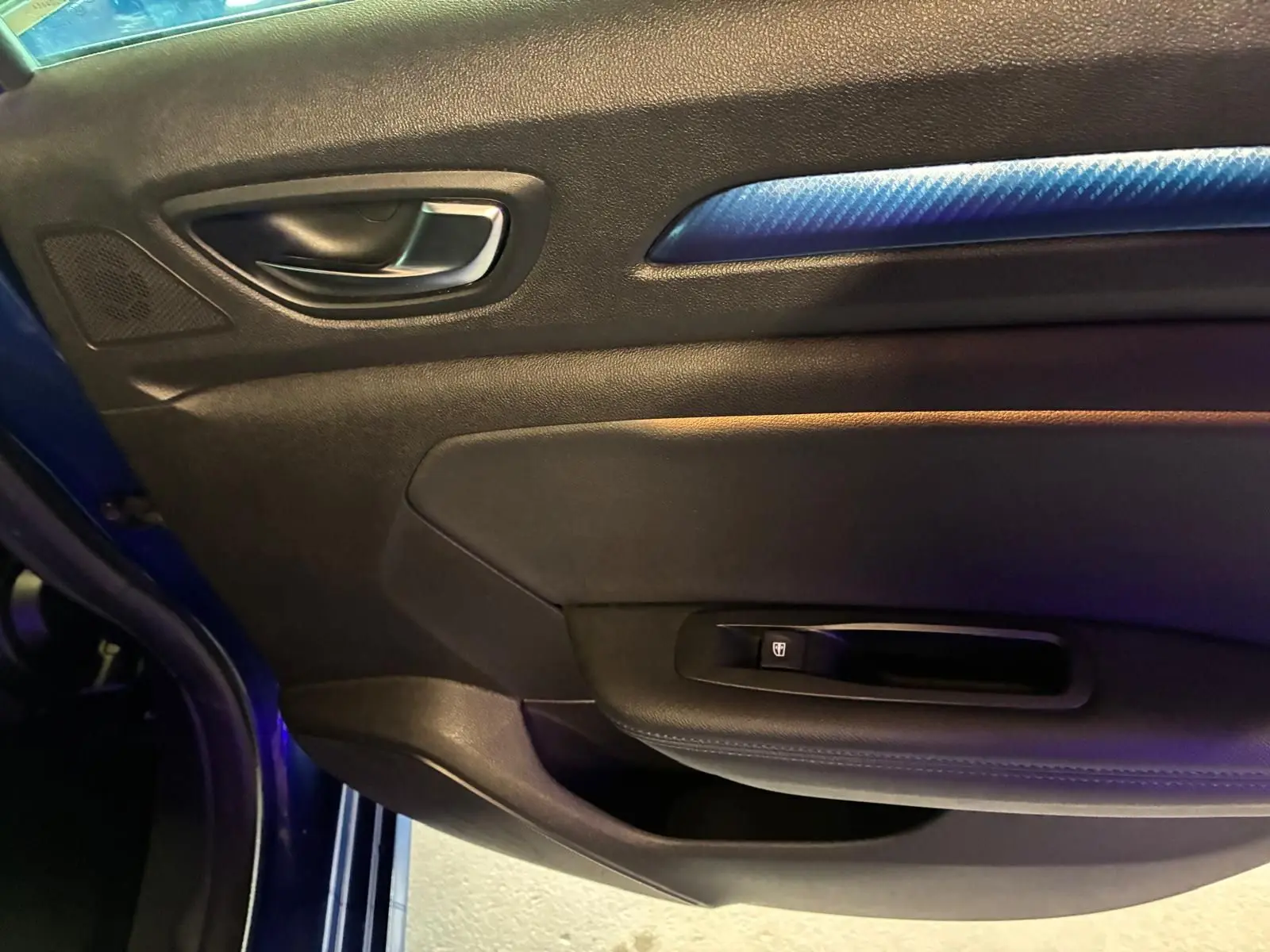 Détail de la porte avant gauche de la Renault Mégane bleu, avec poignée intérieure et insert décoratif bleu.