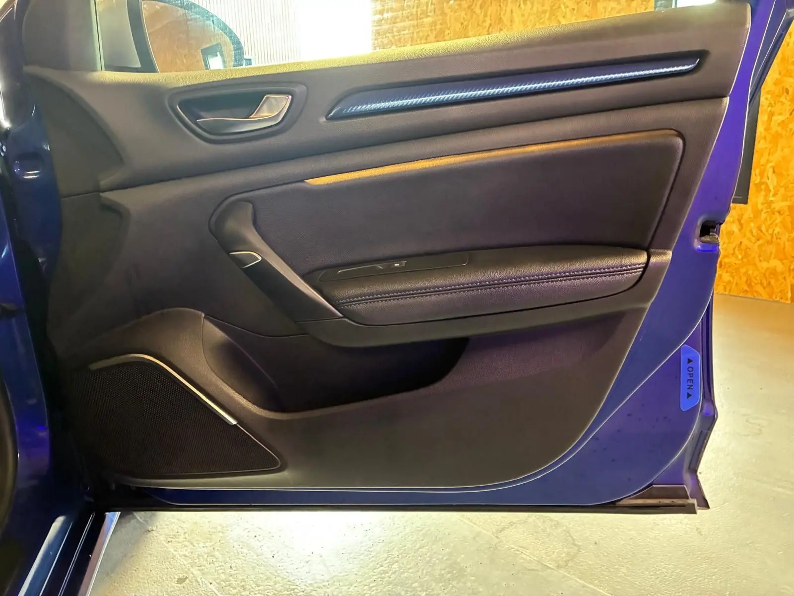 Vue de profil intérieur de la porte avant gauche d'une Renault Mégane bleu 2019 avec garniture noire et poignée argentée.