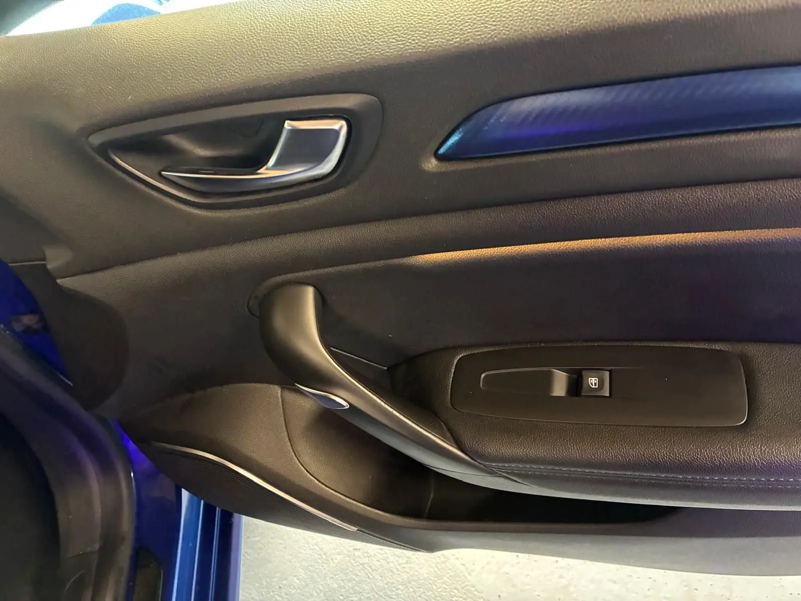 Gros plan sur la porte intérieure côté gauche de la Renault Mégane bleu, avec poignée argentée et insert bleu.