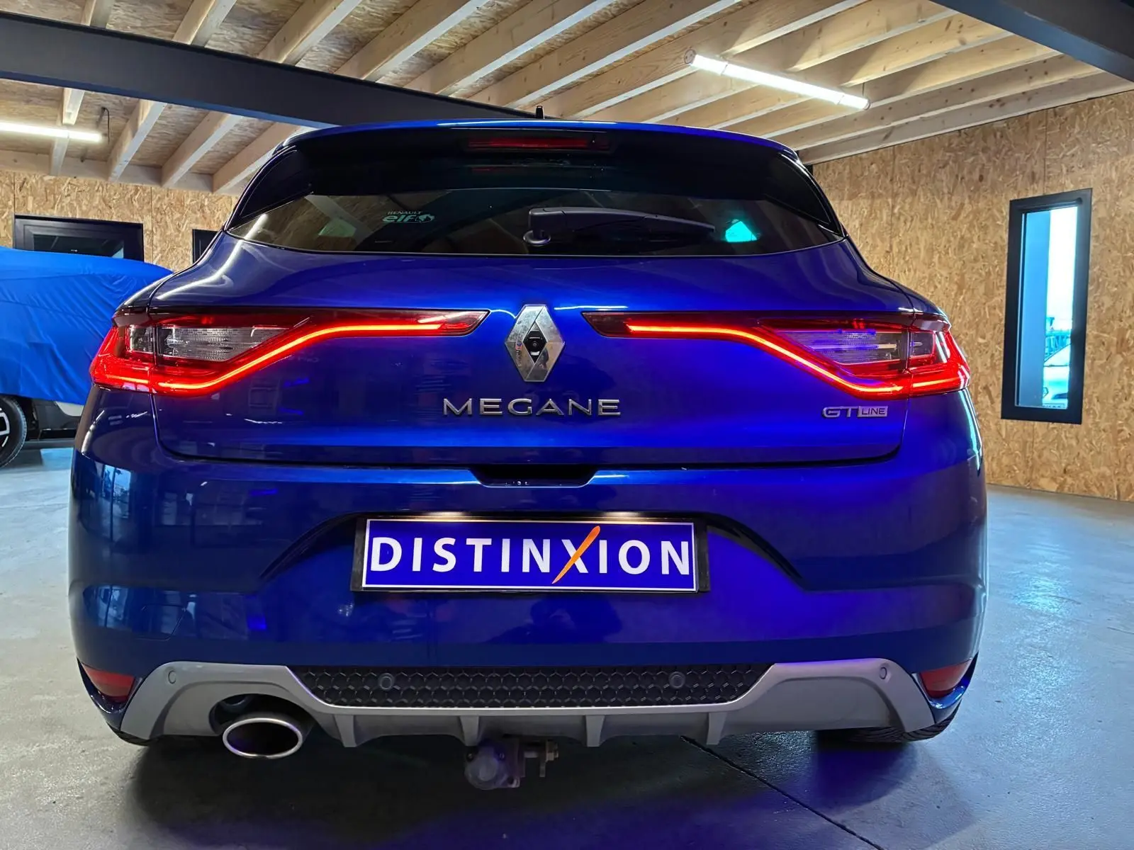 Vue arrière d'une Renault Mégane GT Line bleue 2019 avec feux LED allumés et plaque Distinxion.