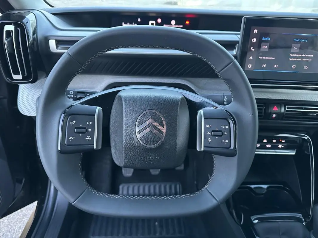 Vue rapprochée du volant noir de la Citroën C3 2025 avec commandes intégrées et tableau de bord numérique.