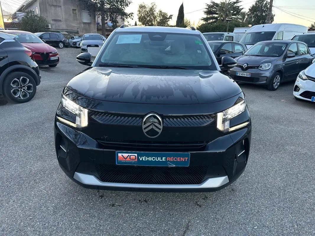 Vue avant d'une Citroën C3 noire 2025 avec phares allumés et logo Citroën bien visible sur un parking.