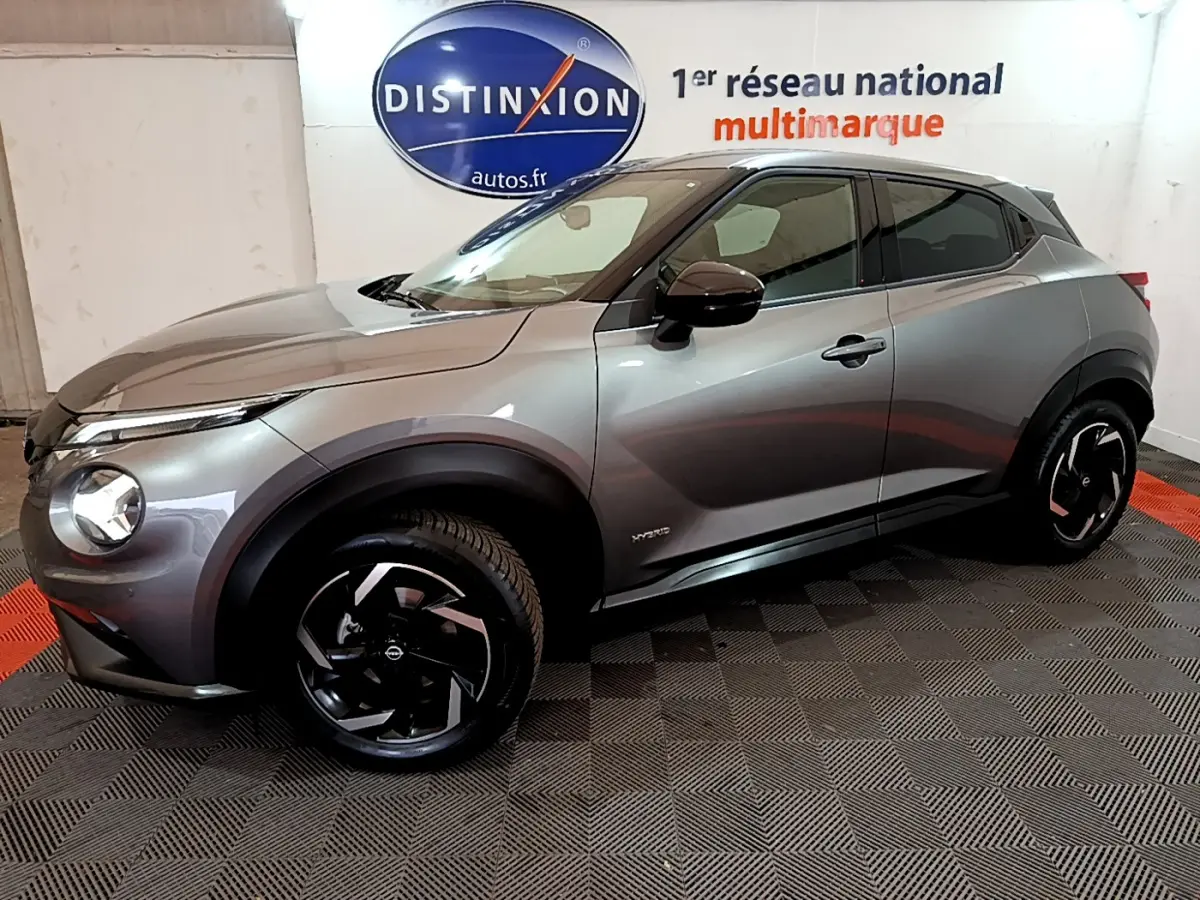 Nissan Juke Hybrid gris foncé vue de profil côté gauche dans un showroom avec jantes noires distinctives.