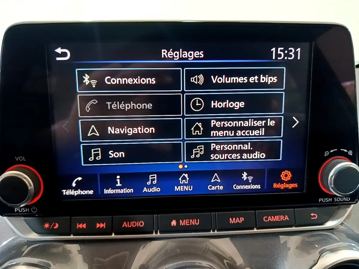 Écran tactile central du Nissan Juke Hybrid 2023 affichant le menu Réglages avec boutons audio et caméra.