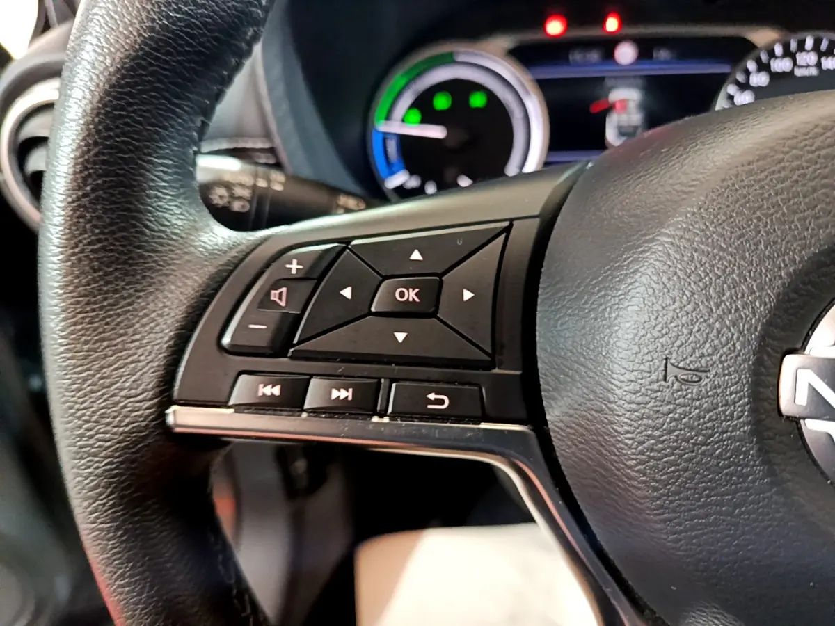 Gros plan sur le volant noir du Nissan Juke Hybrid 143 Business+ 2023 avec commandes multifonctions et tableau de bord lumineux.