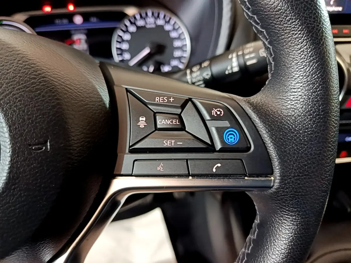 Gros plan sur les commandes du volant cuir noir du Nissan Juke Hybrid 143 Business+ 2023 avec affichage du tableau de bord flou.