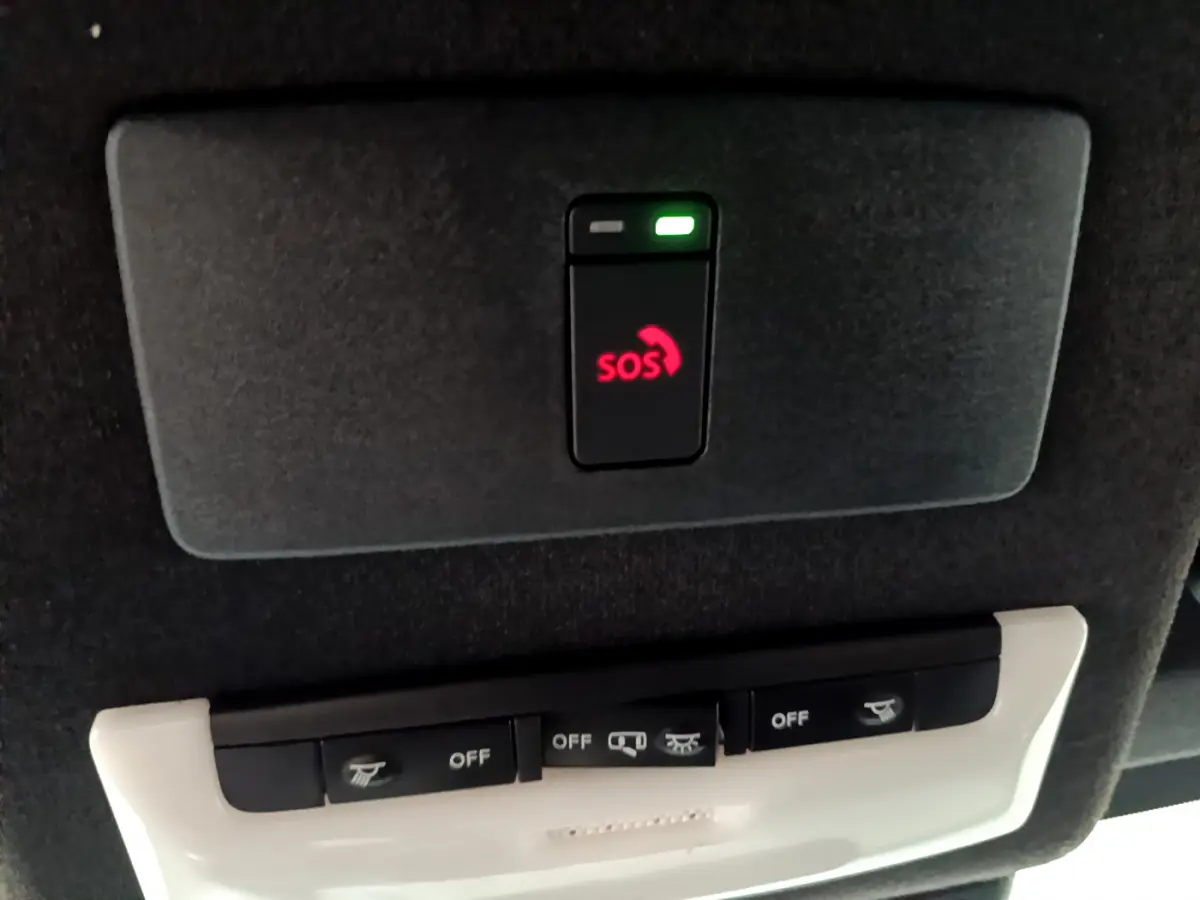 Bouton SOS rouge allumé sur panneau de plafond noir, avec commandes d'éclairage intégrées dans Nissan Juke Hybrid 2023.