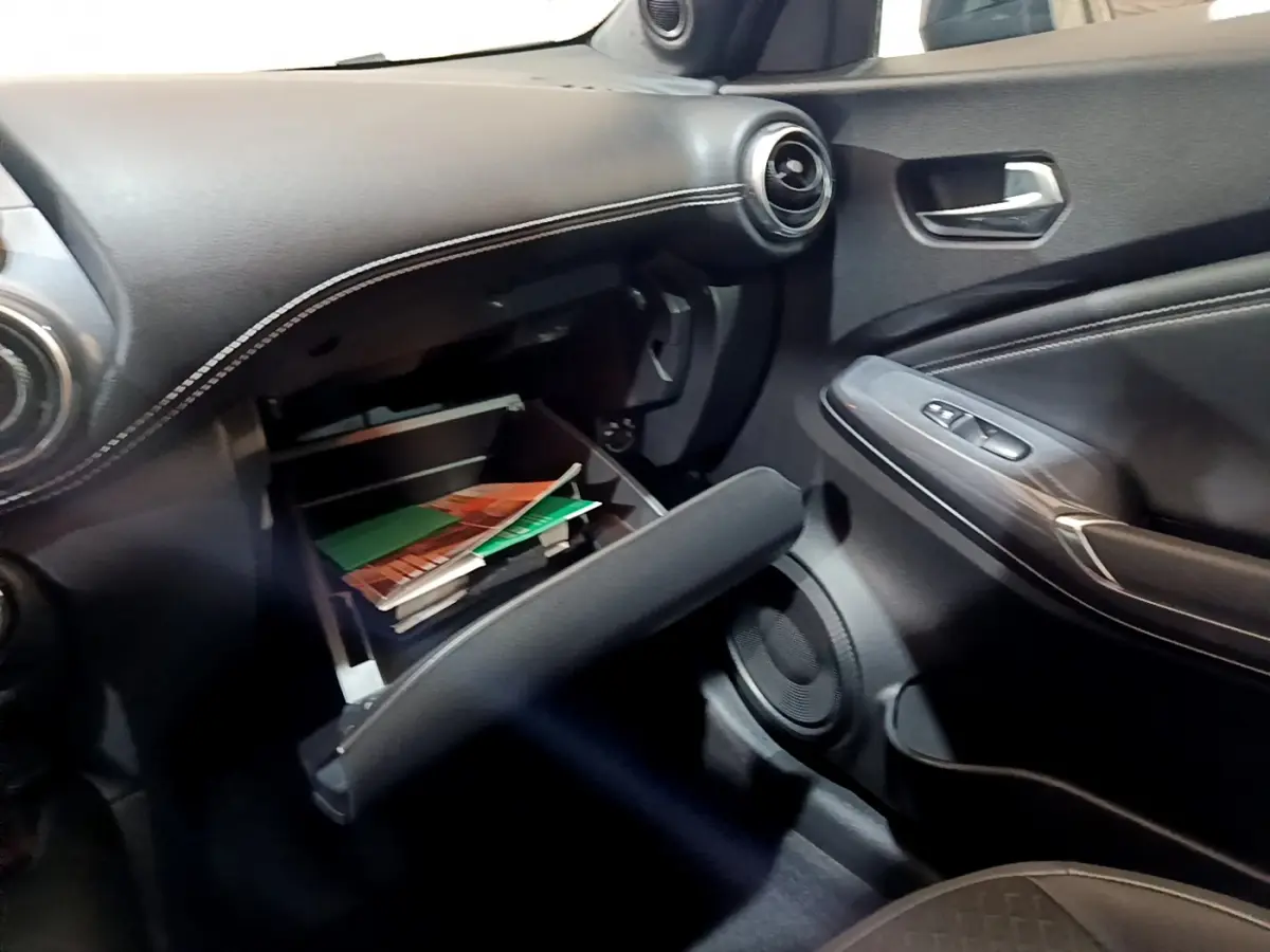 Vue intérieure côté passager du tableau de bord noir avec boîte à gants ouverte contenant des documents dans un Nissan Juke 2023.