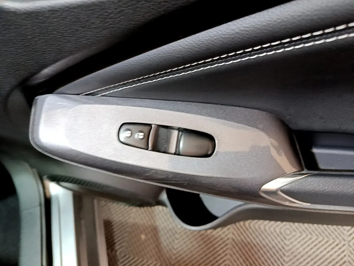 Gros plan sur la commande de verrouillage des portes côté gauche, garniture cuir gris foncé avec surpiqûres blanches.