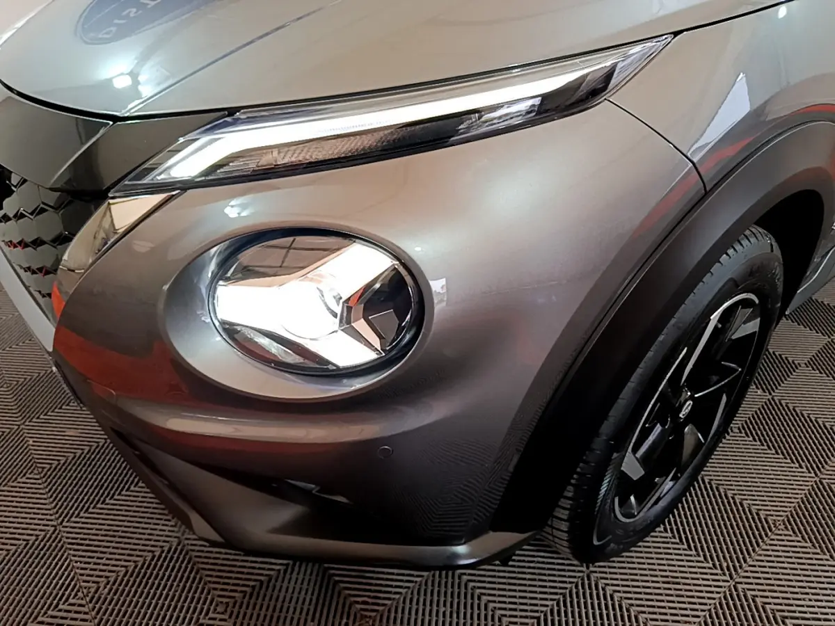 Gros plan sur l'avant droit gris foncé du Nissan Juke Hybrid 143 Business+ avec phare rond et jante noire.