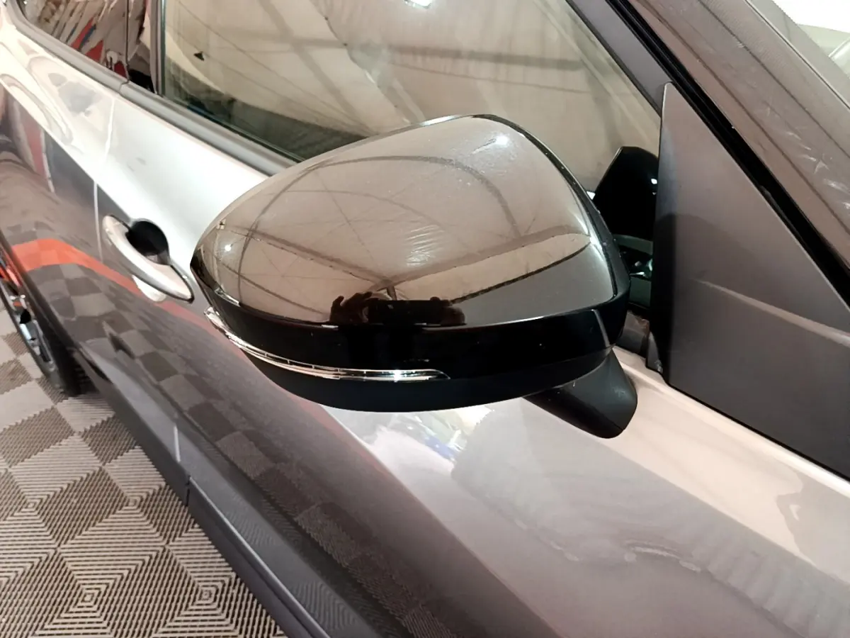 Rétroviseur gauche noir brillant du Nissan Juke Hybrid gris foncé, avec clignotant intégré, vue en gros plan.