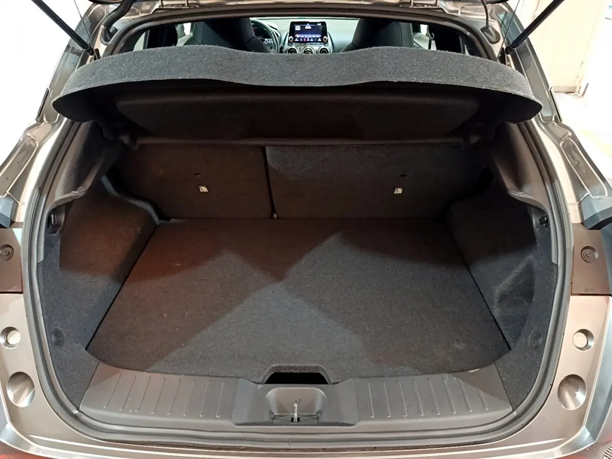 Coffre ouvert vu de l'arrière d'un Nissan Juke Hybrid gris foncé, montrant l'espace de chargement vide.