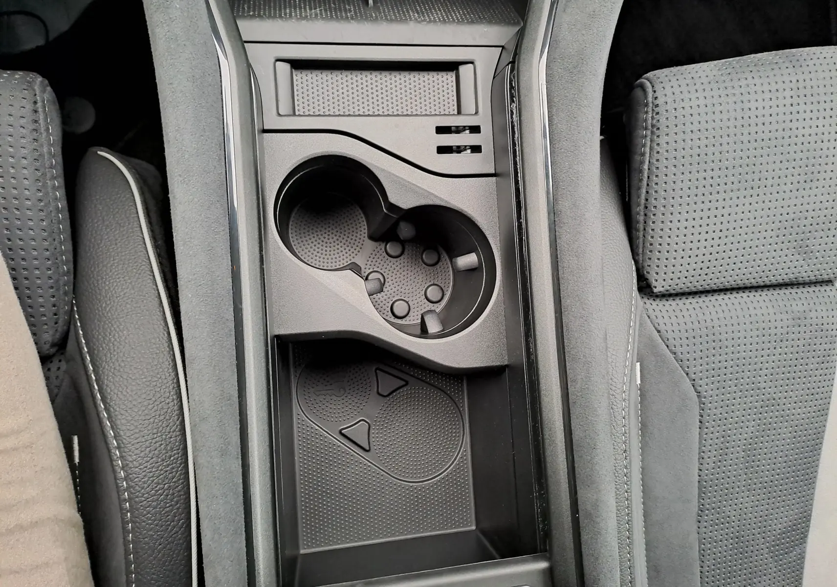 Vue plongeante sur la console centrale noire du Skoda Kodiaq 2025, avec porte-gobelets et rangement entre sièges perforés.