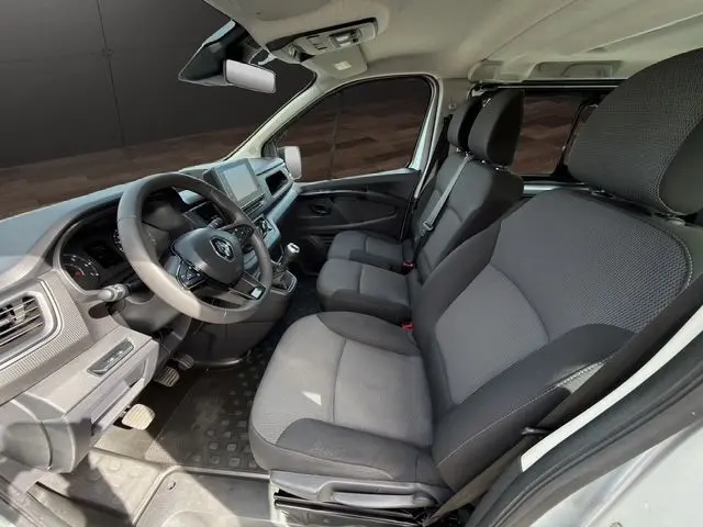 Vue intérieure côté conducteur du Renault Trafic Combi gris platine, montrant les sièges tissu noirs et le tableau de bord moderne.