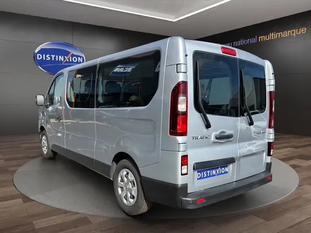Vue 3/4 arrière droite du Renault Trafic Combi gris platine, avec portes arrière vitrées et logo Distinxion visible.